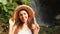 Portrait of young happy smiling mixed race tourist girl in white dress and straw hat with amazing wild jungle waterfall. Lifestyle