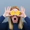 Portrait of young and healthy funny woman with oranges over eyes against gray background