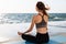 Portrait of young healthy woman sitting in lotos pose while practicing meditation at seaside