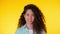 Portrait of young hispanic student girl with curls on yellow background. Trendy cute woman smiling to camera. Studio