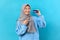 Portrait of young Indonesian woman in hijab pointing bank card wear blue sweater