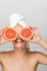 Portrait of young joyful woman without makeup with white towel on head covering eyes with halves of grapefruits over