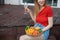 Portrait of young joyful wonderful woman sitting on step of wooden veranda, holding glass of white wine, cut vegetables.