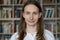 Portrait of young librarian woman smiling looking at camera in library bookshelf background