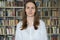 Portrait of young librarian woman smiling looking at camera in library bookshelf background