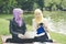 Portrait of young lovely pleasant mix ethnic woman sitting on grass at summer green park and having a discussion