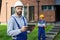 Portrait of young male builder looking at camera while holding digital tablet pc with coworker working in the background