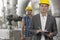 Portrait of young male supervisor writing on clipboard with manual worker in background at industry