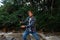 Portrait of a young male videographer with a camera on a stabilizer in his hands stands on a hike near a stream and shoots video