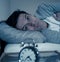 Portrait of young man in bed staring at alarm clock trying to sleep feeling stressed and sleepless