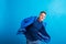 Portrait of a young man with blue anorak in a studio, standing against blue background.