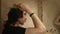 Portrait of young man brushing long layered dark brown hair in bathroom standing in front of mirror, side view, face profile