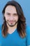 Portrait of a young man with cool long hairstyle looking at camera. Isolated on blue background