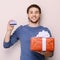 Portrait of young man holding gift box and a credit card. Handsome young smiley man holding a credit card in one hand and a gift