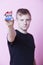 Portrait of a young man holding a VOTE badge up to the camera against pink background