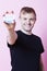 Portrait of a young man holding a VOTE badge up to the camera against pink background