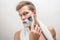 Portrait of young man shaving. He has white foam on beard. Guy is serious and concentrated. Isolated on white background.