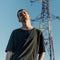 Portrait of a young man wearing an oversized black t-shirt and posing against a transmission towe