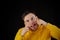 Portrait of young man in yellow hoodie with grimacing face. Close up of funny guy monkeying on black background.