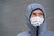 Portrait of young man in zipped gray hoodie and home made cotton face mouth virus mask, only eyes visible, gray wall in background