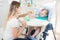 Portrait of young mother feeding her baby son sitting in highchair