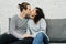Portrait of young multiethnic couple kissing on couch at home in the living room. People, love and friendship concept