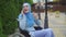 Portrait young muslim woman disabled in a traditional scarf communicates on a smartphone sitting in a wheelchair in the