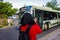 Portrait of young Muslim woman standing on sidewalk taking photo of passing bus