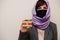 Portrait of young muslim woman wearing formal wear, protect face mask and hijab head scarf, hold Suriname flag card against