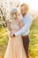 Portrait of young nice-looking couple in blossoming garden, standing near the flowering tree and hugging on a sunny day