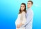 Portrait of young pair pending the kid isolated on blue background, Young attractive couple: pregnant mother and happy father,