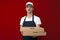 Portrait of a young pizza delivery man in uniform on a red background, a courier guy gives boxes of pizza