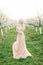 Portrait of young pretty blond woman in wedding elegant dress in the flowered garden in the spring time. Fruit trees