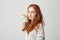 Portrait of young pretty ginger girl with freckles looking at camera touching hair over white background.