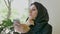 Portrait of young pretty muslim woman in hijab sitting in cafe, holding phone and looking forward, concerned and