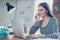 Portrait of young pretty smiling secretary sitting at the table, working with computer and receiving calls