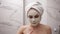 Portrait of young pretty woman with white towel on head is applying fresh white thick mask and scrub on the face