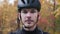 Portrait of young professional cyclist in fall beautiful forest. Extra close up view of male face in helmet puts on sport glasses