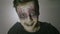 Portrait of a young psychopath zombie man with strange eyes and face paint doing frightening halloween moves -