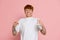 Portrait of young red-headed angry man in white t-shirt isolated over pink studio background. Concept of youth, fashion