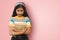 Portrait of young relaxed indian asian girl posing isolated tilting head forward down looking downwards and hugging books