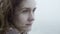 Portrait of young sad woman in foggy day looking afar and dreaming. Brunette hair of pensive female waves on the wind.