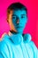 Portrait of young serious boy, student or teen looking at camera isolated on magenta studio backgroud in neon. Human