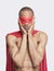 Portrait of young shirtless man in superhero costume with hands on face against gray background