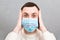 Portrait of young shocked sick man in medical mask with coronavirus word at gray cement background. Respiratory protection.