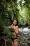 Portrait Young slender girl posing in the jungle hiding behind a palm leaf. Wildlife and a girl