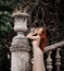 Portrait of young slim sensual woman tourist at ancient stone flowerpot on stairs balustrade handrail in old garden