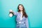 Portrait of young smile puzzled woman student in denim clothes hold alarm clock isolated on blue background. Time is running out.