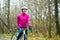 Portrait of Young Smiling Female Cyclist in Pink Jacket Resting with Road Bicycle in the Cold Sunny Autumn Day