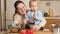 Portrait of young smiling mother feeding her baby son with fruit puree on kitchen. Concept of little chef, children